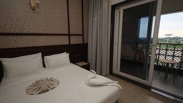 Habitación de hotel con una cama grande, vistas al exterior y un balcón con mobiliario.
