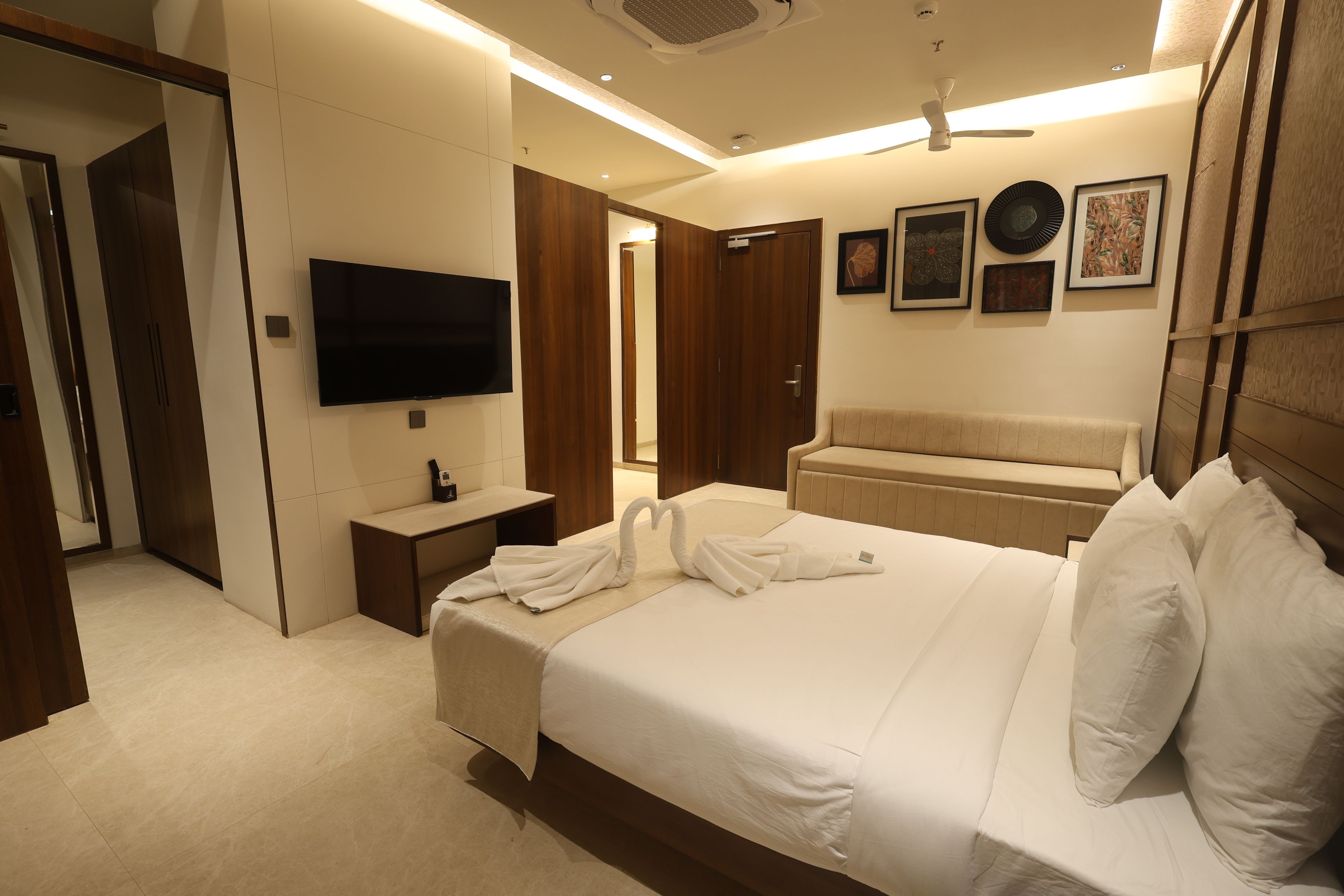 Habitación de hotel con una cama grande, televisor de pantalla plana, mesita de noche, espejo, sofá y una pared decorada con obras enmarcadas.