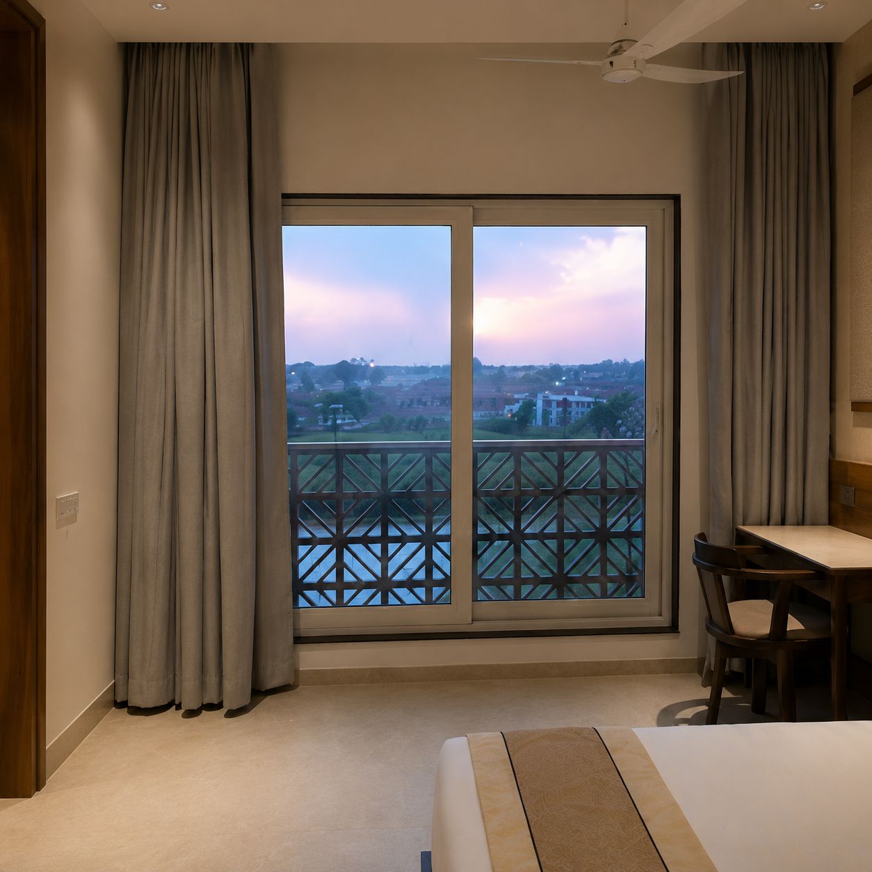 A hotel room with a large sliding glass door leading to a balcony, a bed, a desk, and a chair.