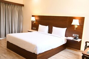 A hotel room with a large bed, wooden headboard, bedside lamps, a small table, and a telephone. - Mastiff Villa Camellia, Palampur (Palampur)