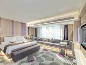 Quarto de hotel moderno com uma cama grande, um sofá, uma TV e uma janela ampla.