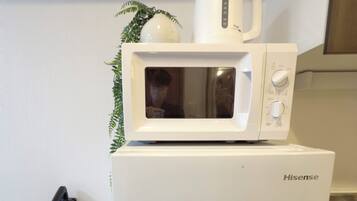 A compact kitchen with a white Hisense microwave on top of a white refrigerator, a small potted plant, and a visible power outlet.