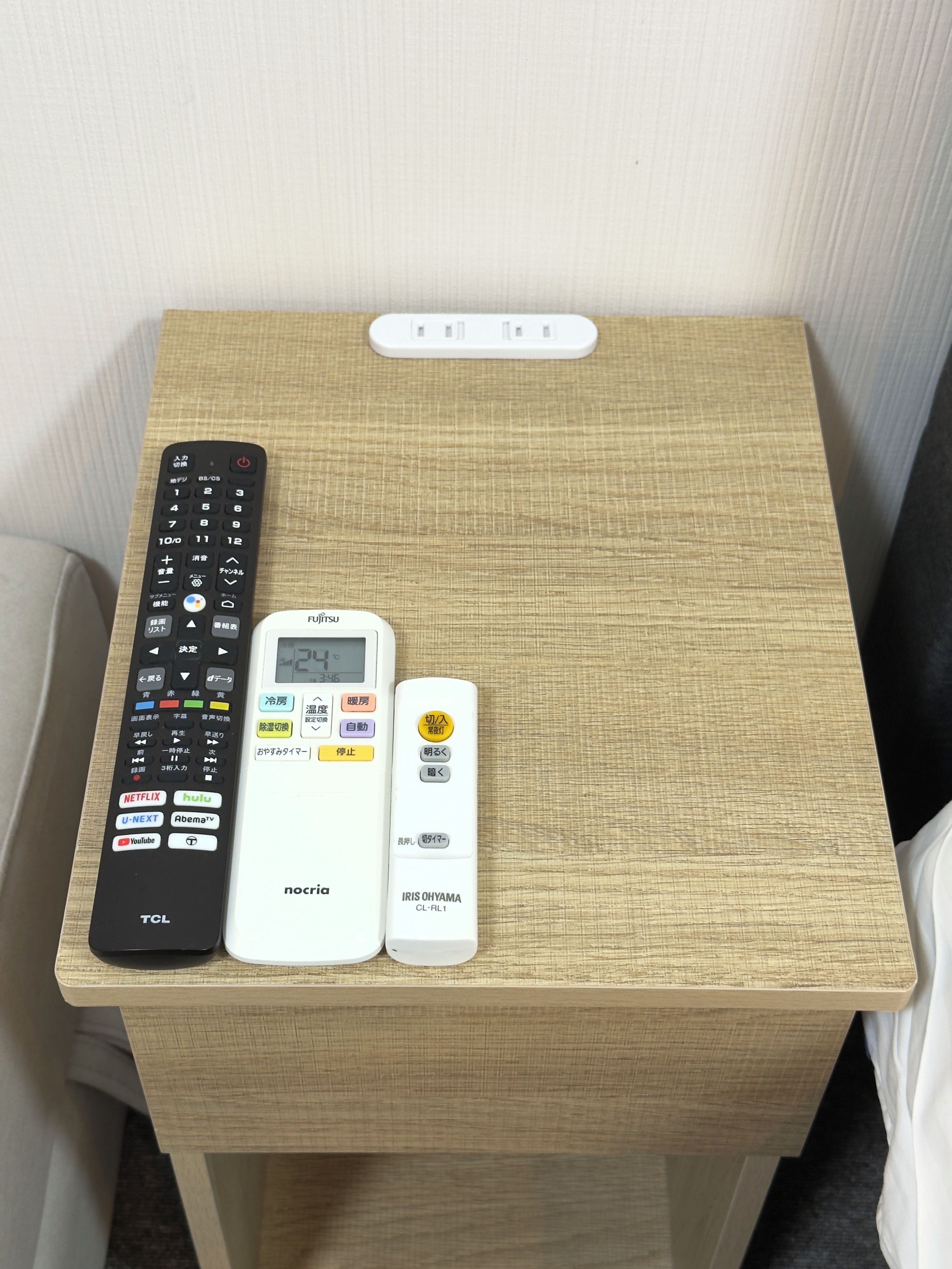Una mesa de madera con un control remoto negro, un termostato blanco y otro control remoto blanco.