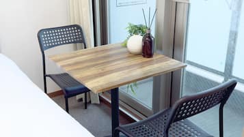 A small balcony with a wooden table, two chairs, a potted plant, and a vase with a candle.
