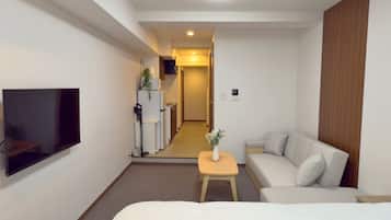 A hotel room with a bed, a TV mounted on the wall, a small table with a vase, and a sofa.
