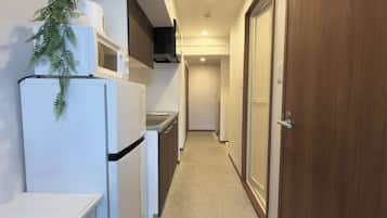 A narrow hallway with a refrigerator, microwave, and sink on one side, and a wooden door on the other.