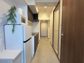 Un pasillo estrecho con un refrigerador, un microondas y un lavamanos a un lado, y una puerta de madera al otro.