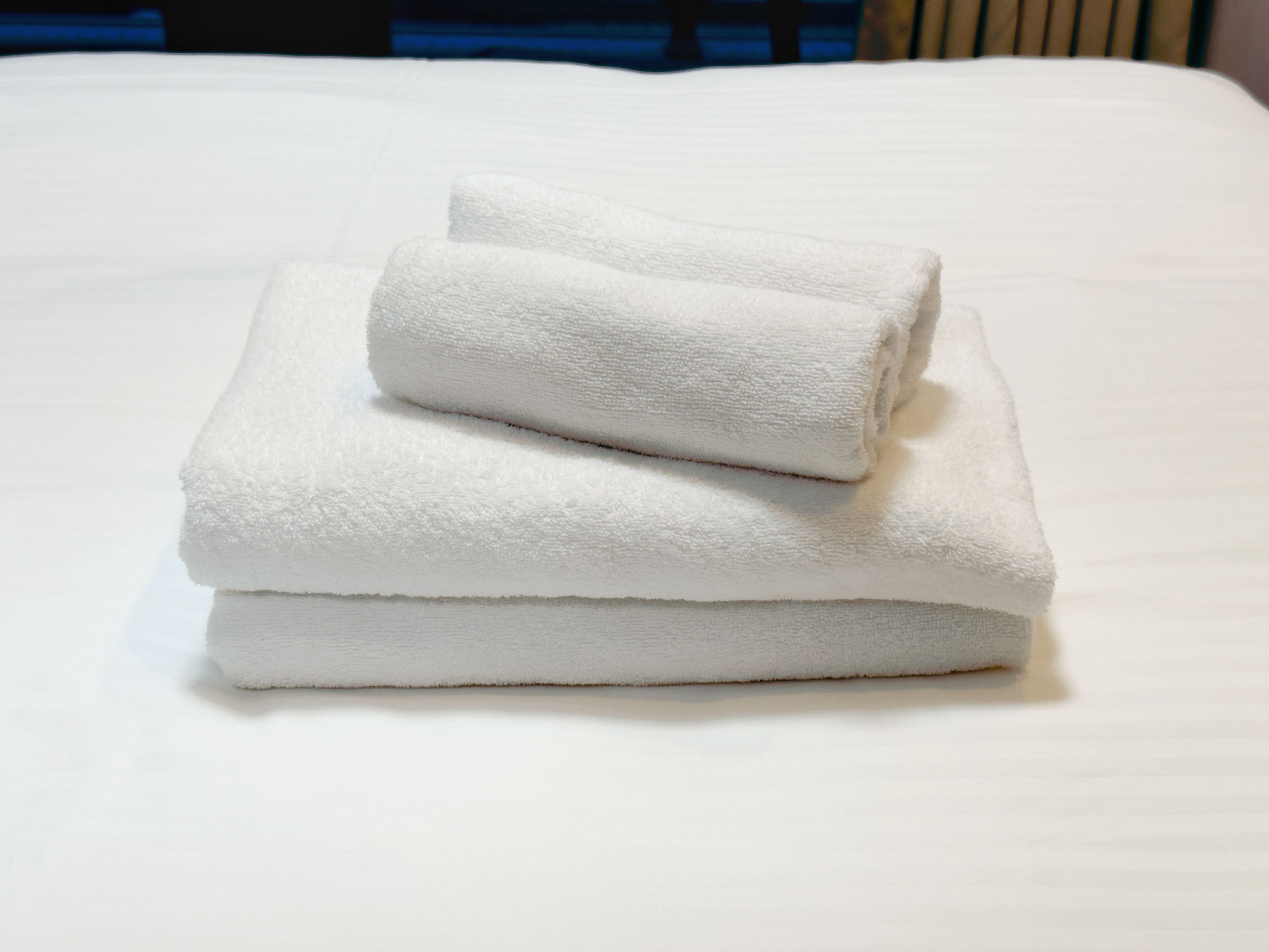 A neatly folded white towel stacked on a white bed.