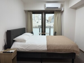 Una habitación de hotel con cama, una mesita de noche con control remoto, una ventana con cortinas y un equipo de aire acondicionado.