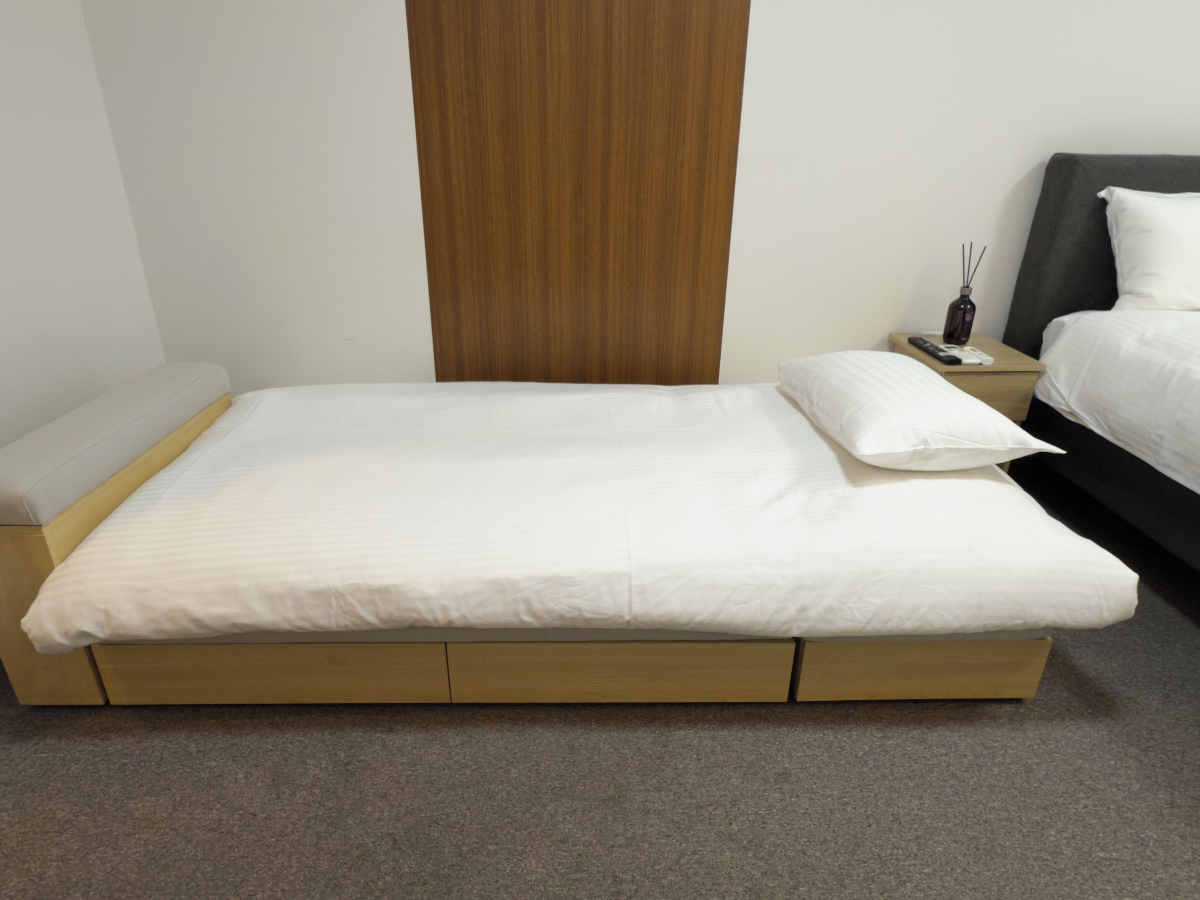Habitación estándar de hotel con una cama individual, una mesita de noche con control remoto y un cabecero de madera.