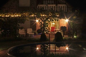 Ein Backsteinhaus mit überdachter Terrasse, Sitzgelegenheiten im Freien und einem Swimmingpool.