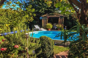 Ein Schwimmbad mit Gazebo, umgeben von üppiger Vegetation und einem gepflegten Garten.