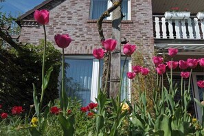 Un edificio de ladrillo con un balcón blanco y un jardín de tulipanes rosados.