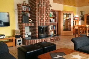 Una sala de estar con chimenea de ladrillo, una estantería, un televisor y un comedor con sillas de madera.