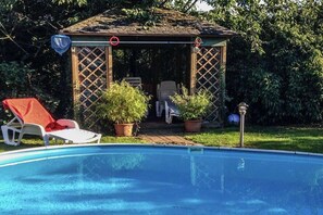 Piscina con zona de estar cubierta, sillones de descanso y plantas en macetas.