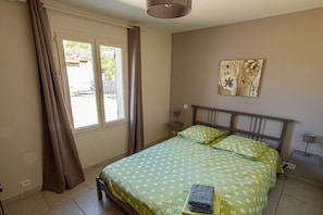 Ein Schlafzimmer mit einem Bett, Vorhängen, einem Fenster, einem Nachttisch und Wandbildern.