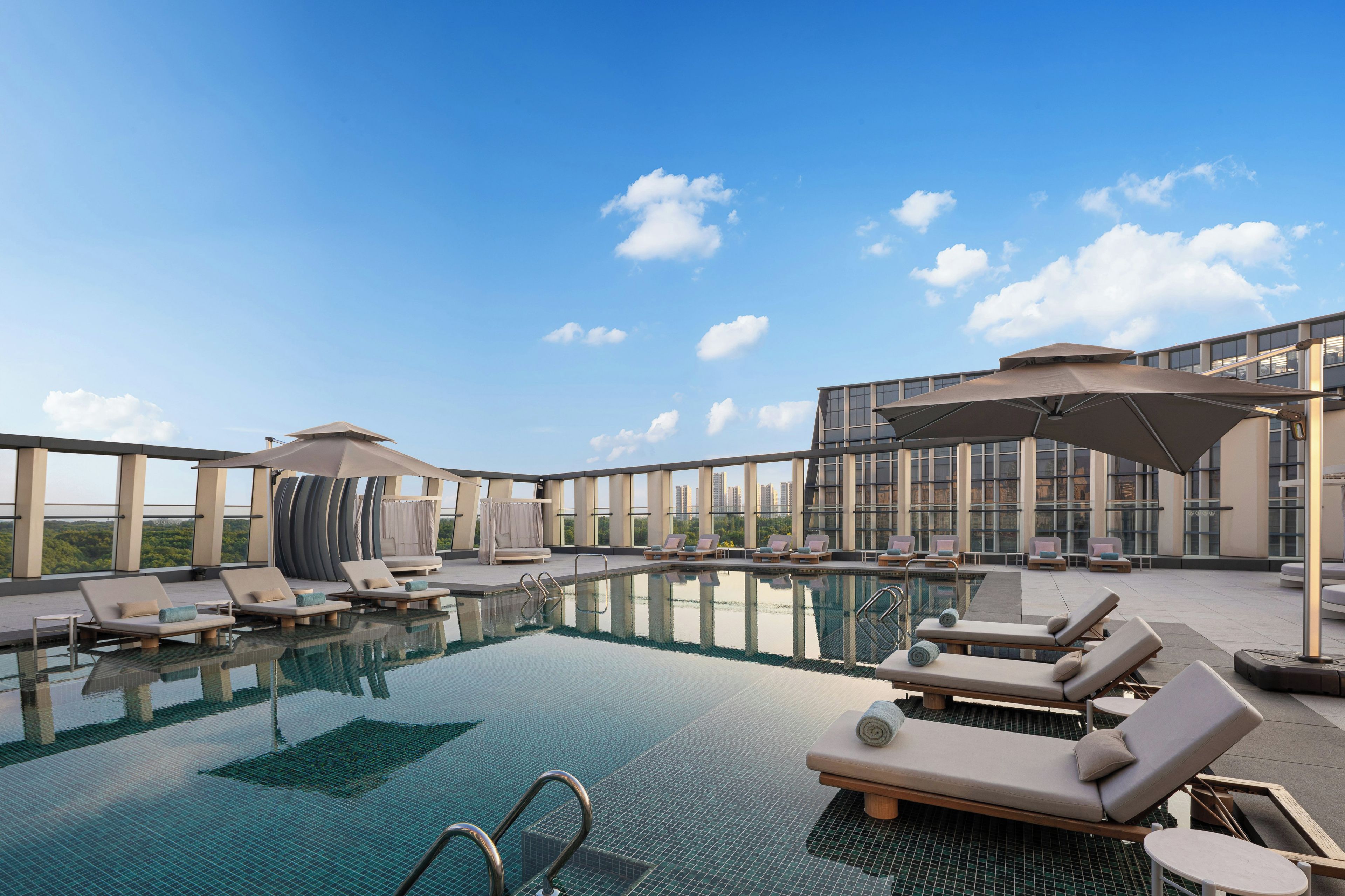 Una piscina infinita con sillones de descanso y sombrillas, con vista a un paisaje urbano.