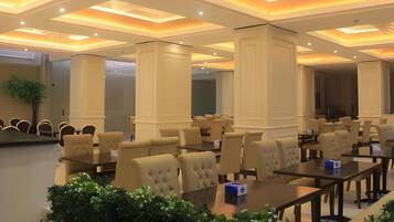 A hotel conference room with multiple tables and chairs, recessed lighting, and a large chandelier.