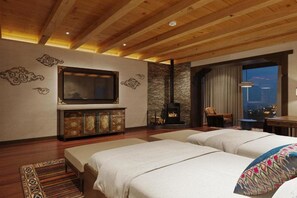 A hotel room with a fireplace, a television, a sofa, and a view of the city at night. - Taj Gangtey Resort & Spa, Bhutan (Wangdue Phodrang)