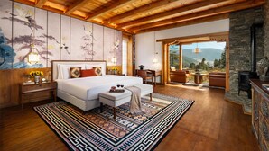 A spacious bedroom with a large bed, a wooden ceiling, a stone fireplace, and a view of the mountains. - Taj Gangtey Resort & Spa, Bhutan (Wangdue Phodrang)
