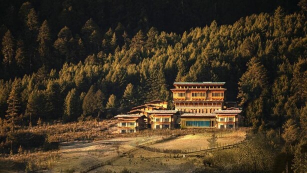 A traditional multi-story building with a symmetrical facade, surrounded by dense forest. - Taj Gangtey Resort & Spa, Bhutan (Wangdue Phodrang)