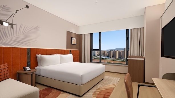 Habitación de hotel con una cama grande, un escritorio y vistas a la ciudad.