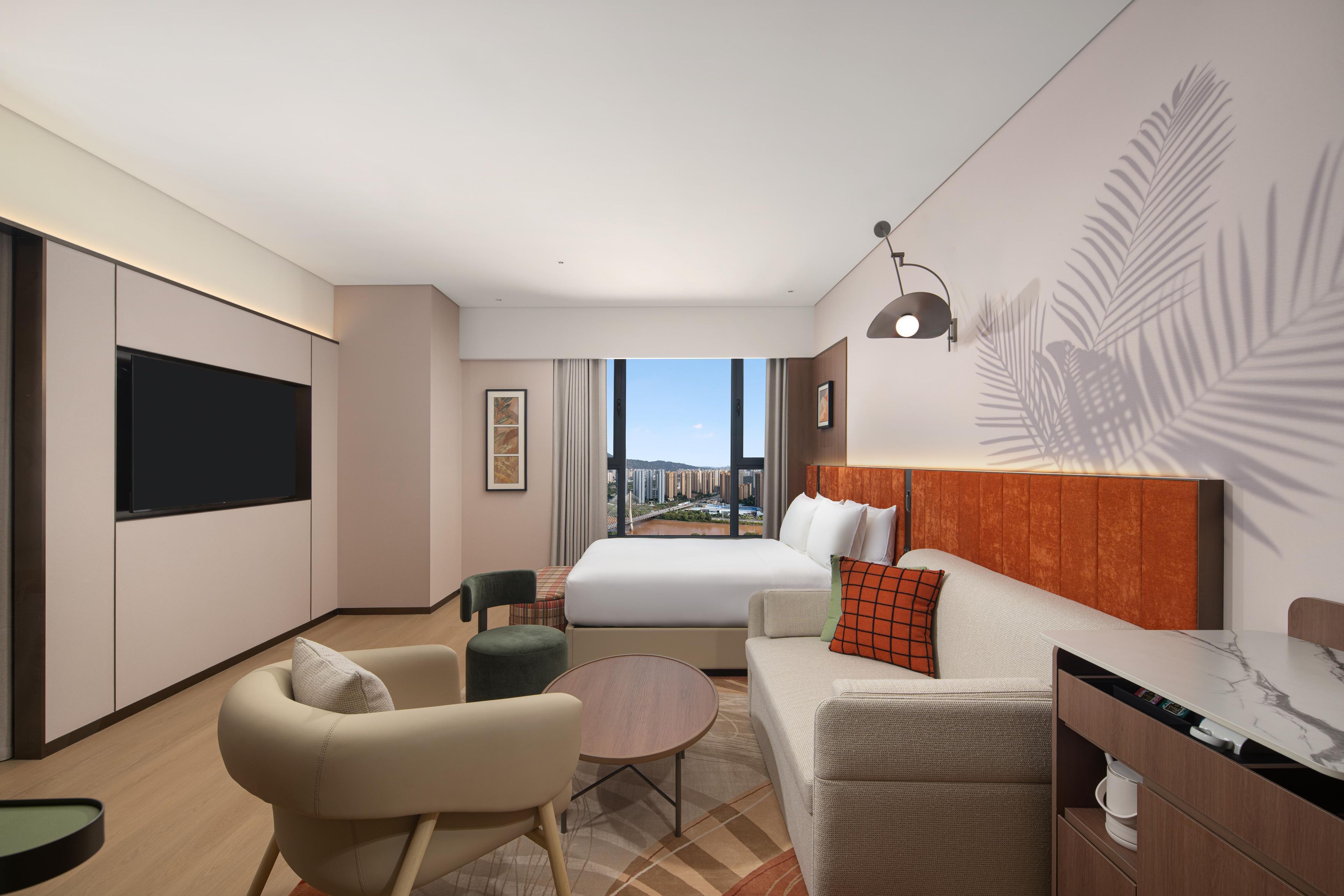 A modern hotel room with a large bed, a sofa, a desk, and a TV.
