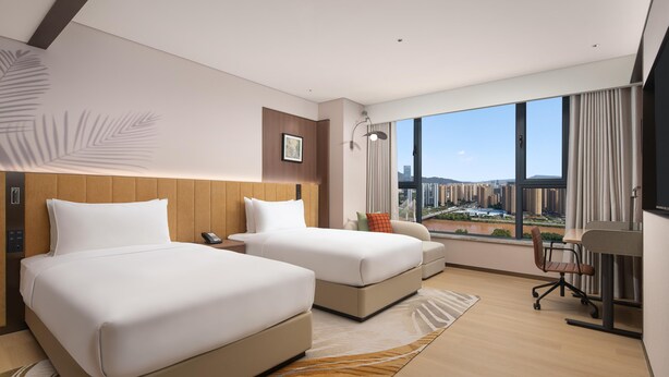 A hotel room with two beds, a desk, and a view of a cityscape. - Hilton Garden Inn Lanzhou Anning (Lanzhou)