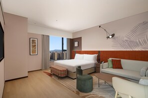 Una habitación de hotel moderna con una cama grande, un sofá, una mesita y vistas a la ciudad.