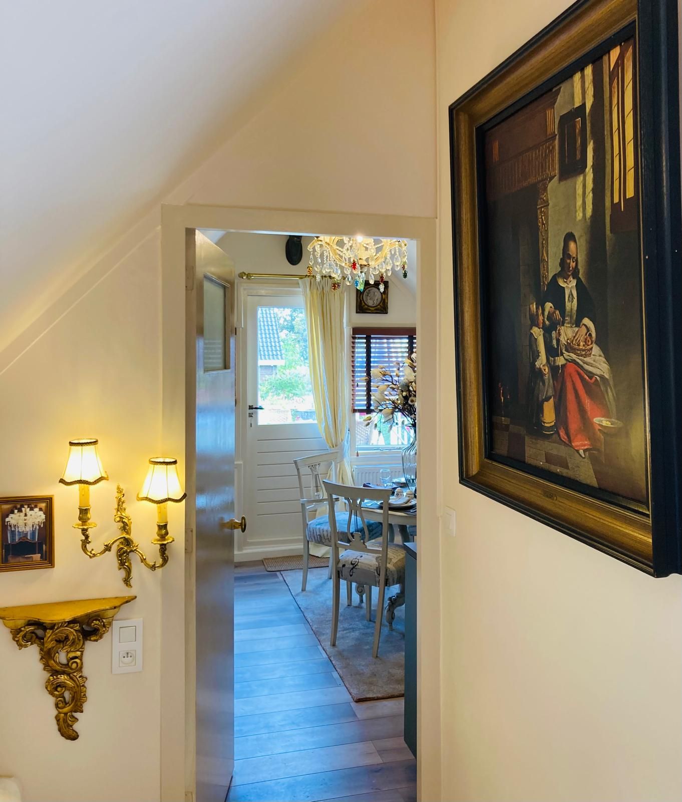 A hallway with a dining area, a chandelier, and a framed painting.
