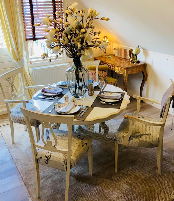 Une table à manger dressée pour quatre personnes, agrémentée d’un vase de fleurs et entourée de chaises d’époque.