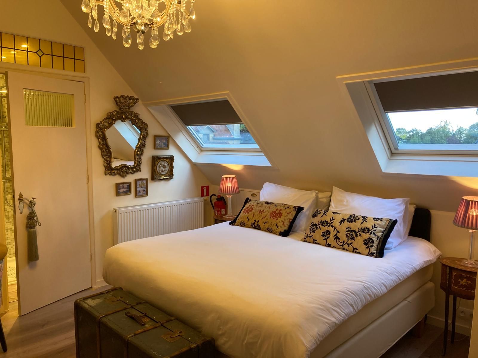 Ein Schlafzimmer mit einem großen Bett, Dachfenstern, einer Kristallleuchtre und einer Heizung.
