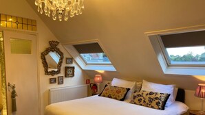 Une chambre à coucher avec un grand lit, des fenêtres de toit, un lustre et un radiateur.