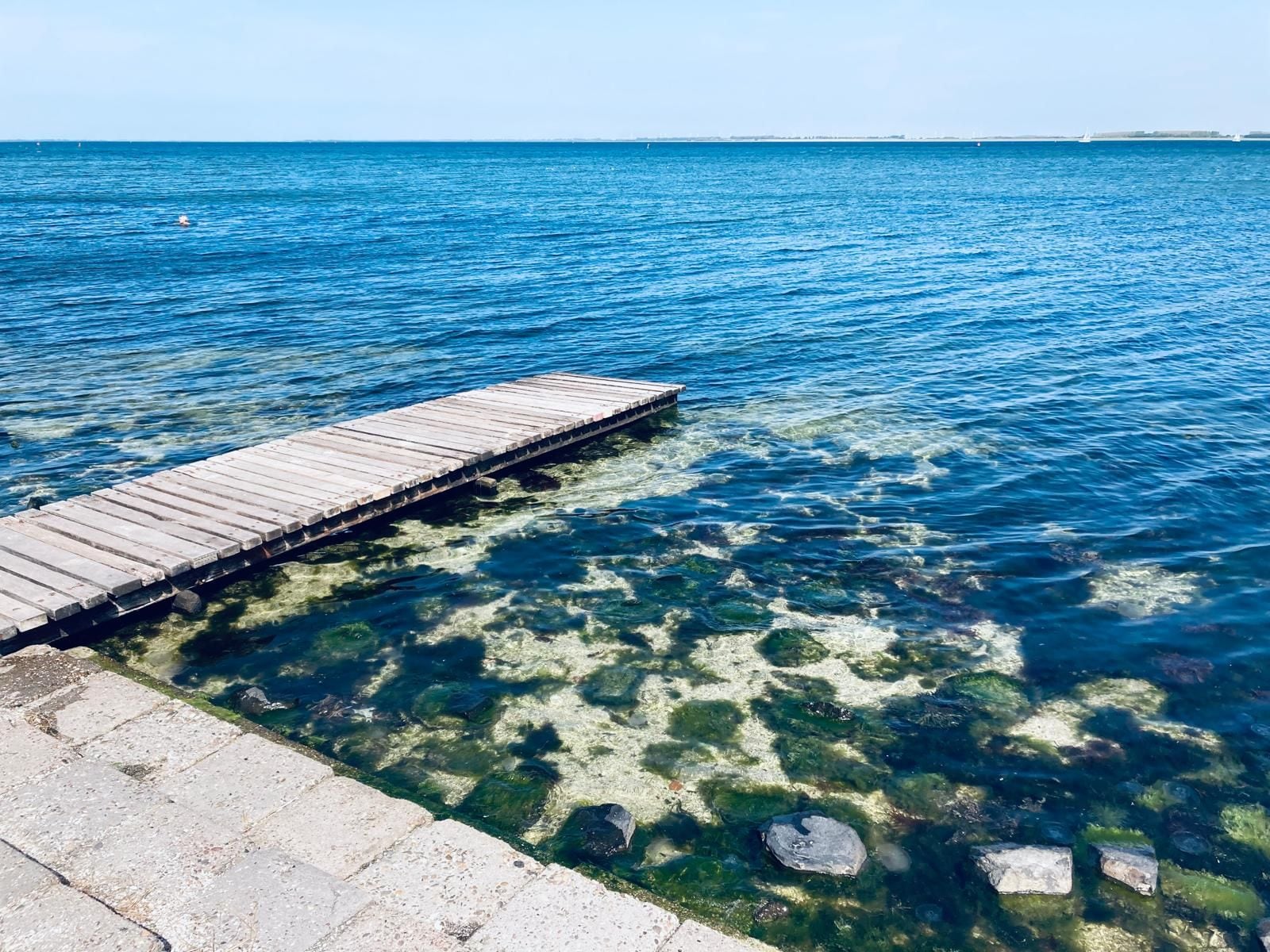 A wooden pier extending into clear blue water with visible rocks beneath the surface.