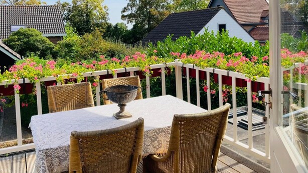 Une terrasse avec une table et des chaises, un grand parasol et une vue sur une maison et un jardin.