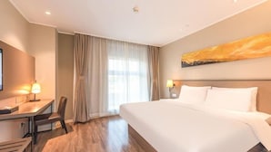 Habitación de hotel con una cama grande, un escritorio con silla, un televisor y una ventana con cortinas.