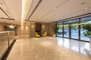 A modern lobby with a reception desk, seating area, and large windows offering a view of the street. - Homeinn Plus (Beijing)