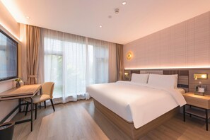 A hotel room with a large bed, a desk with a chair, a TV, and a bedside table with a lamp. - Homeinn Plus (Beijing)