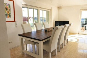 A dining area with a wooden table and white chairs, a television on the wall, and a large window with a view. - Holiday home with 2 bedrooms (Sasbachwalden)