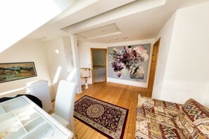 A spacious loft with a high ceiling, a large window, a wooden floor, a patterned rug, and a colorful abstract painting. - Holiday home with 2 bedrooms (Sasbachwalden)