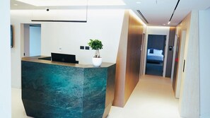 A modern hotel reception area with a reception desk, a potted plant, and a hallway leading to a bedroom. - Arbnor Hotel (Tirana)