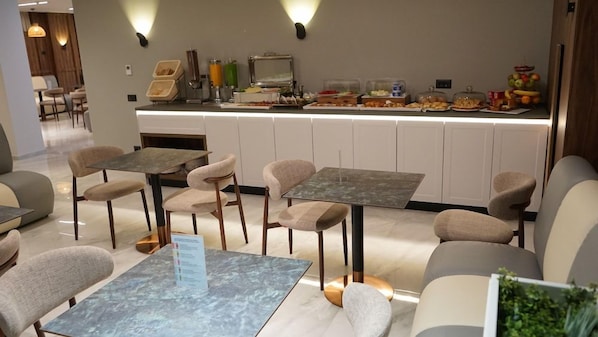 A hotel dining area with tables and chairs, a buffet counter with food items, and a reception desk. - Arbnor Hotel (Tirana)