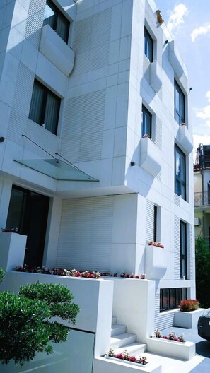 A modern building with a flat facade, large windows, and a balcony with potted plants. - Arbnor Hotel (Tirana)
