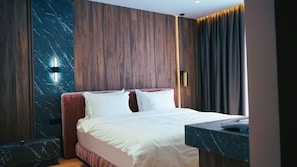 A modern hotel room with a large bed, dark wood paneling, marble accents, and a view of the city. - Arbnor Hotel (Tirana)