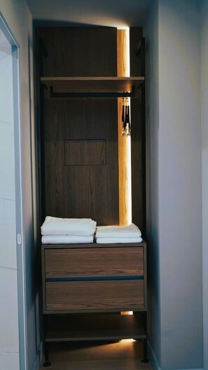 A compact, walk-in closet with a wooden wardrobe, a hanging rod, and a bed with neatly folded white linens. - Arbnor Hotel (Tirana)