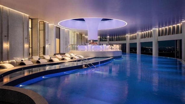 Una piscina interior moderna amb zona de bar, gandules i vista a la ciutat de nit.