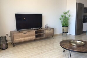 Ein modernes Wohnzimmer mit Fernseher, Holzschrank, rundem Couchtisch und einer Topfpflanze.
