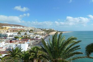 A coastal town with buildings along the beach, palm trees, and a clear sky. - Holiday apartment with 2 bedrooms (Morro jable)