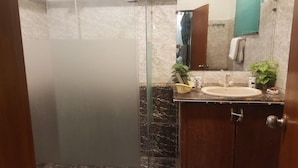 A bathroom with a glass shower enclosure, a sink with a mirror, and a wooden cabinet. - Seashell Inn Hotel (Karachi)