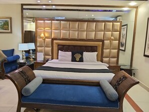 A hotel room with a large bed, a sofa, a nightstand, and a lamp. - Seashell Inn Hotel (Karachi)